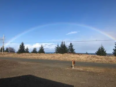 a rainbow in the sky over a road at Sunrise Cabin secluded beach front accommodation in Sandspit