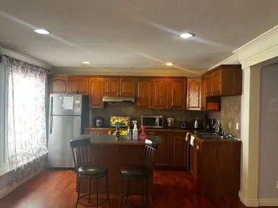a kitchen with wooden cabinets and a kitchen island with bar stools at Hamptons Rose garden family! in Calgary