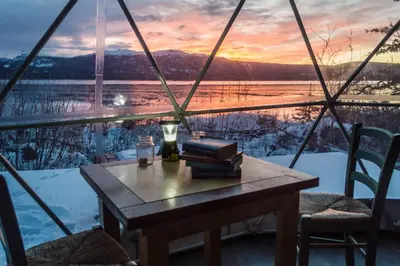 a table with books on top of a balcony with a sunset at Little Atlin Lodge in Tagish