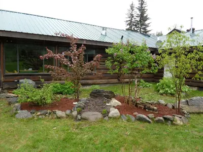 a garden with two trees in front of a house at Summit River Lodge & Campsites in Valemount