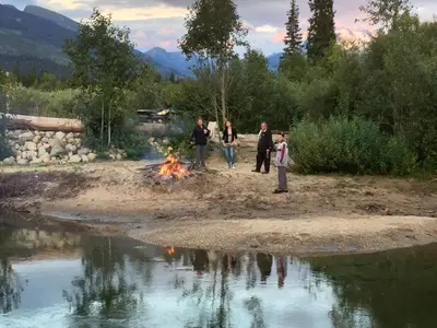 a group of people standing around a fire next to a pond at Summit River Lodge & Campsites in Valemount