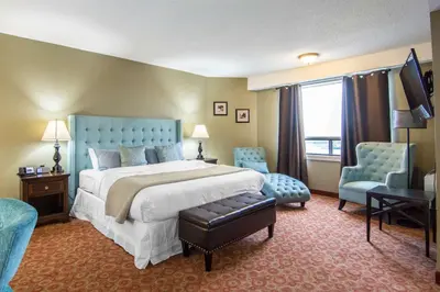 a bedroom with a large bed and two blue chairs at Quality Hotel in Drumheller