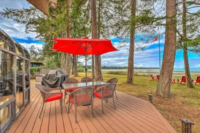 a table and chairs with a red umbrella on a deck at Kye Bay Beach House by EMR Vacation Rentals in Comox
