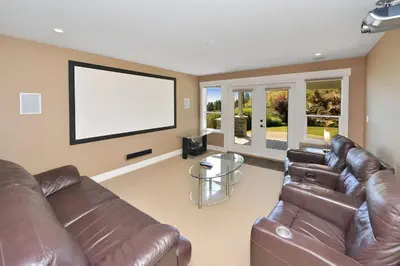 a living room with a leather couch and a large screen at Nature's Gate Executive Estate by EMR Vacation Rentals in Victoria