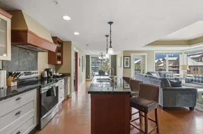 an open kitchen and living room with a couch at Sunset Ridge - Luxurious Corner Condo - Spectacular Mt Views with open Pool! in Canmore