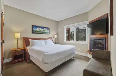 a bedroom with a bed and a television and a chair at Sunset Ridge - Luxurious Corner Condo - Spectacular Mt Views with open Pool! in Canmore
