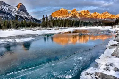 a river in the snow with mountains in the background at Rundle Rise - Spacious Condo Steps from Main Street in Canmore