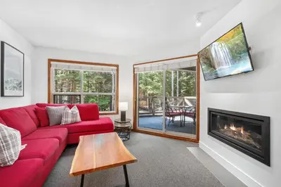 a living room with a red couch and a fireplace at 2BR in The Aspens, Ski In, Ski Out, Pool and Hot Tub, Gas Fireplace, Ski Valet, Gym in Whistler