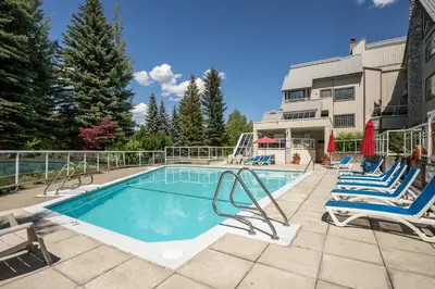 a swimming pool with lounge chairs and a building at 2BR plus Loft in Wildwood Lodge, Free Ski Bus, Hot Tub and Pool, Private Patio, Parking in Whistler