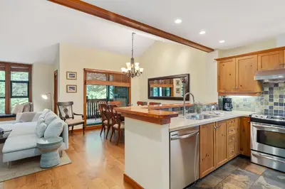 a kitchen with wooden cabinets and a living room at 3BR in The Woods, Private Hot Tub, Wood Burning Fireplace, King Ensuite, Private Garage in Whistler