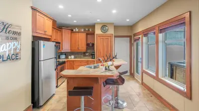 a kitchen with wooden cabinets and a stainless steel refrigerator at I Spy - Cozy Pet Friendly, Ski In Ski Out Condo with Private Hot Tub in Big White