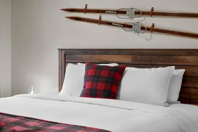 a bed with a red and black plaid pillow on it at Newly Renovated Grizzly Lodge, Spacious 3BR 2BA with open pool, hot tub in Canmore