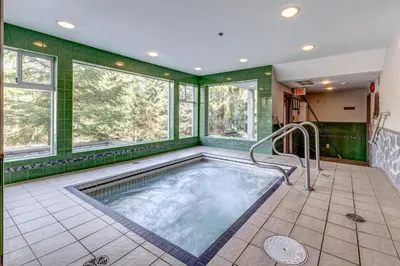 a hot tub in a room with green walls and windows at Greystone Lodge 408 Luxury in Whistler