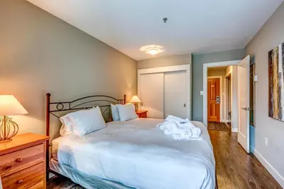 a bedroom with a large white bed with a wooden dresser at Greystone Lodge 221 Ski-in Out in Whistler