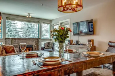 a dining room with a table with plates and wine glasses at Greystone Lodge 221 Ski-in Out in Whistler