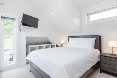 a white bedroom with a bed and a flat screen tv at West Coast Luxury Living in Vancouver