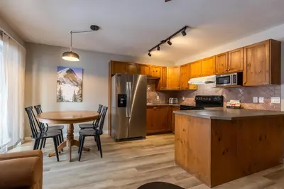 a kitchen with wooden cabinets and a table with chairs at Riverside Condos by Fernie Central Reservations in Fernie