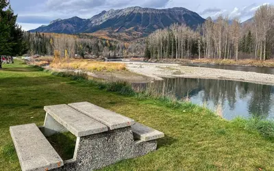 a stone bench sitting on the grass next to a river at Riverside Condos by Fernie Central Reservations in Fernie