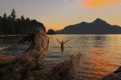 a man standing in a body of water with his arms up at Porteau Cove Olympic Legacy Cabins in Furry Creek