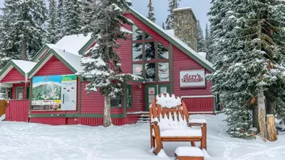 a red building with a chair in the snow at Forest Lane Hideaway - Luxurious Family Friendly Home w Private Hot Tub in Big White