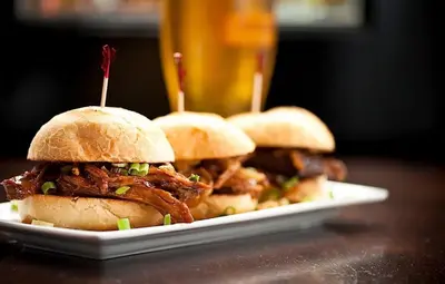 three pulled pork sandwiches on a plate with a drink at The St. Regis Hotel in Vancouver