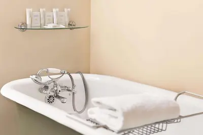 a white bath tub with a towel on a shelf at The Plaza Hotel Downtown, Trademark Collection by Wyndham in Kamloops