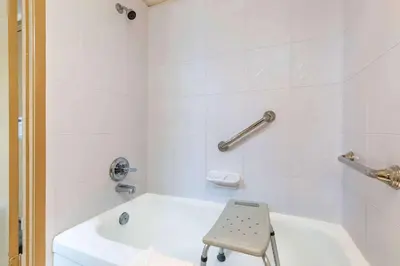 a white bathroom with a white tub and a chair at Ramada by Wyndham Coquitlam in Coquitlam