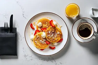 a plate of pancakes with strawberries and a cup of coffee at Sheraton Suites Calgary Eau Claire in Calgary