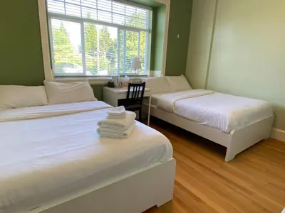 two beds in a room with a desk and a window at Victory House in Burnaby