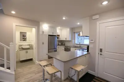 a kitchen with white cabinets and a counter and chairs at Vancouver Traveller Cottage in Vancouver