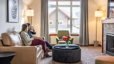 two people sitting on a couch in a living room with a fireplace at Blackstone Mountain Lodge by CLIQUE in Canmore