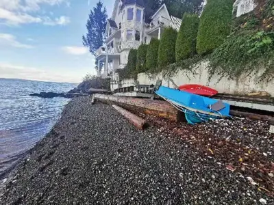 a blue boat sitting on a rocky beach next to a house at Walkon Waterfront Castle Cove Inn in Chemainus