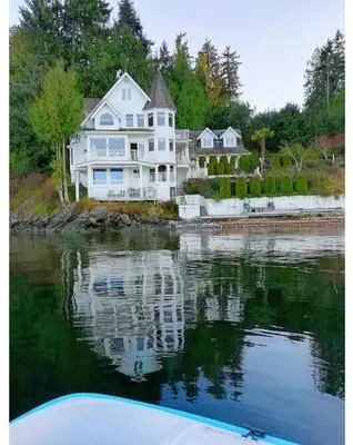 a large white house sitting on top of a body of water at Walkon Waterfront Castle Cove Inn in Chemainus