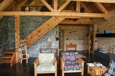 a living room with wooden ceilings and a stone wall at LDR Lodge - Last Dollar Ranch in Smithers