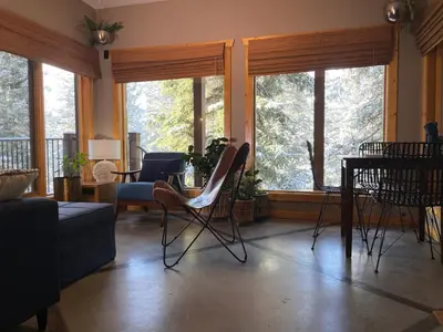 a living room with chairs and a table and windows at Blanchard Mountain BnB in Canmore
