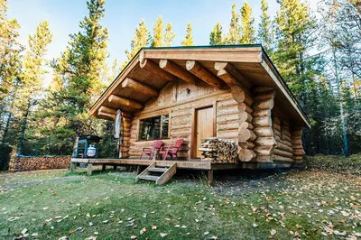 a log cabin with two chairs and a table at Rocky Mountain Escape Dome & Log Cabin Rentals - Rock Lake in Rock Lake Provincial Park