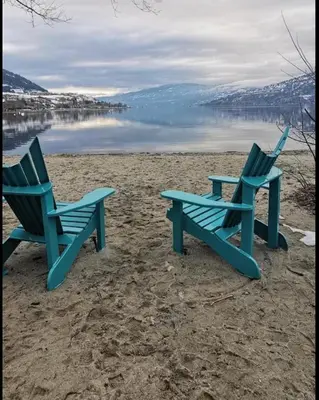two blue chairs sitting on a beach near the water at Vita Resort Vernon on Lake Okanagan in Vernon
