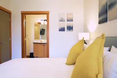 a bedroom with a white bed with yellow pillows at Mtn View Escape with King Size Bed with Outdoor Pool - Banff Pass Included! in Canmore