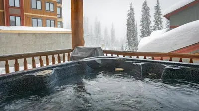 a hot tub on a porch in the snow at Mountain Time - Spacious w Private Hot Tub and an Amazing View in Big White