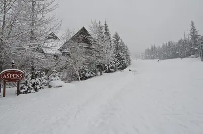 a snow covered street with a sign and trees at Aspens on the Mountain Ski In Out in Whistler