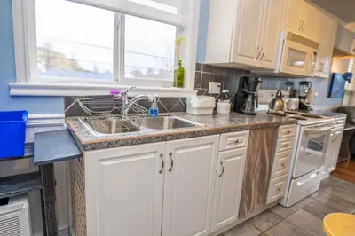 a kitchen with white cabinets and a sink and a window at Downtown Whitehorse Apartment in Old Town in Whitehorse