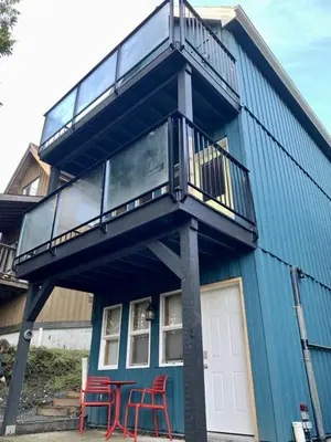 a blue house with two red chairs and a balcony at Kingfisher, Newly Renovated Suite on Ocean Inlet in Ucluelet