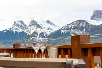 two wine glasses on a table with mountains in the background at Spacious Penthouse Suite-King Beds-Pool & Hot Tub in Canmore
