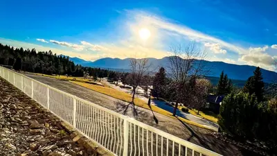 a white fence on a road with mountains in the background at Mountain View Suites by StayIn in Fairmont Hot Springs