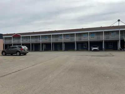 a building with two cars parked in a parking lot at Parkside Inn in Grande Prairie