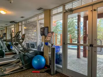 a gym with cardio equipment and a glass door at Sunny Tranquil Woods Turret in Falcon Crest Lodge in Canmore