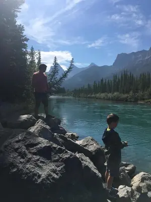 a man and a boy fishing on a river at Alluring Mountain View Condo - Right In The Heart Of Downtown - managed by Little Sister Getaways in Canmore