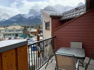 a balcony with a table and chairs and mountains at Alluring Mountain View Condo - Right In The Heart Of Downtown - managed by Little Sister Getaways in Canmore