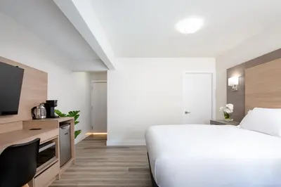 a white bedroom with a bed and a tv at Harrison Grand Motel in Harrison Hot Springs
