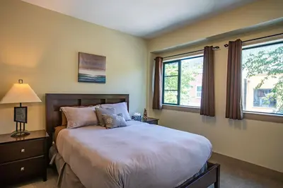 a bedroom with a large bed and two windows at Selkirk Snug by Revelstoke Vacations in Revelstoke